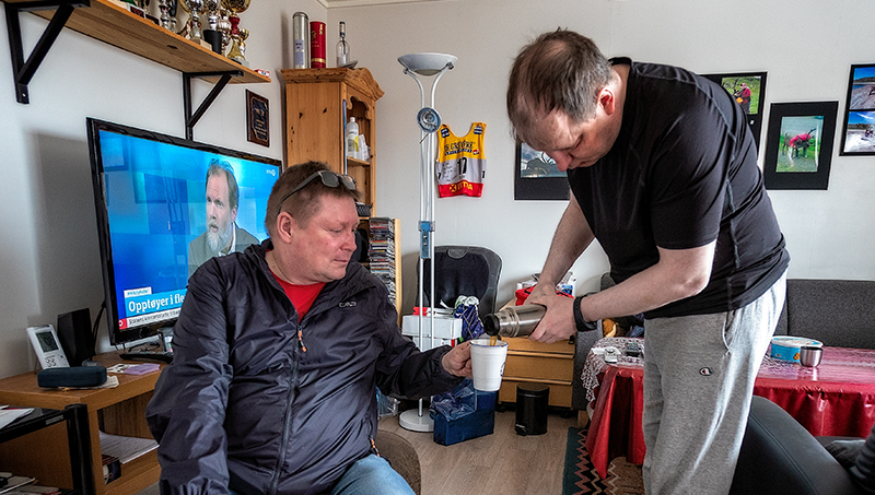 Stående mann skjenker kaffe til en annen mann fra en termos.