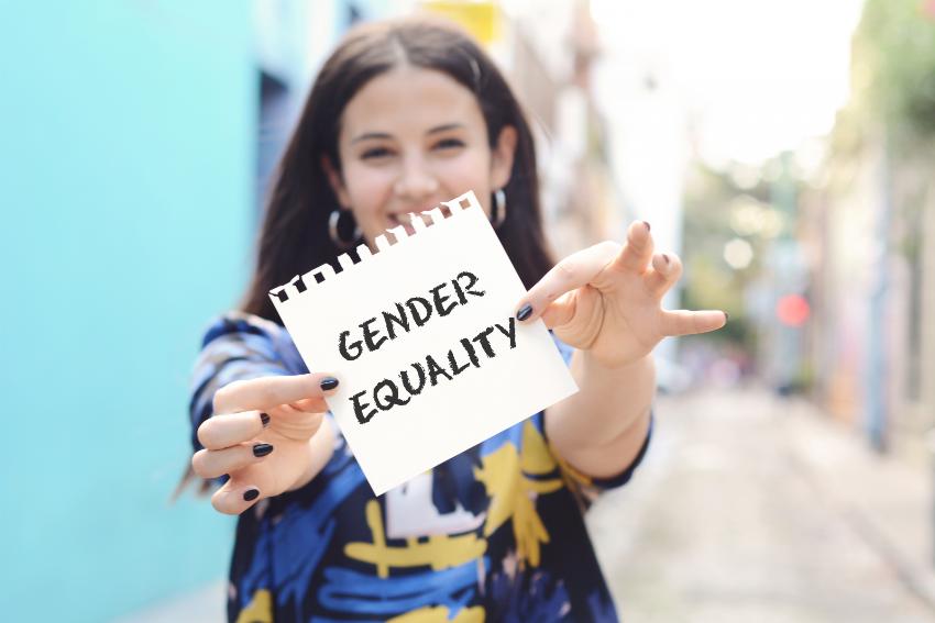 Closeup of a young woman outdoors showing a notepad with the text gender equality written in it. 