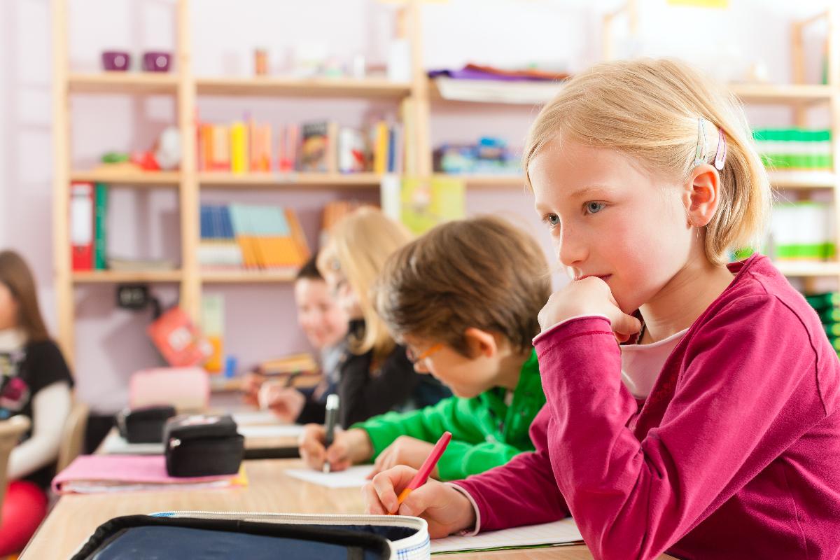 Jente p&aring; skolen, tenkende p&aring; pulten sin