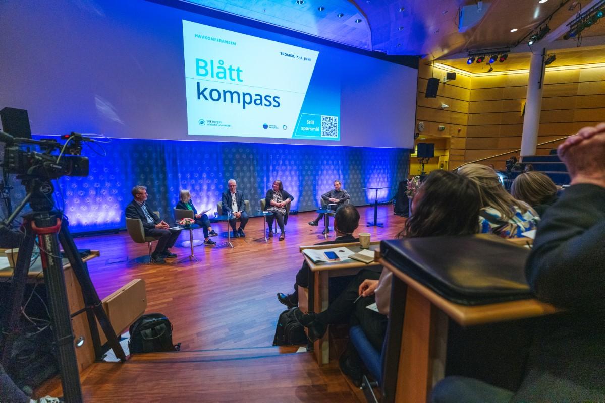 Publikum i eit auditorium ser p&aring; ein paneldebatt. Det st&aring;r Bl&aring;tt kompass p&aring; veggen. Til venstre eit videokamera.