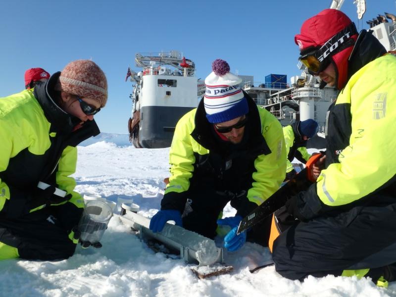 Tre godt kledde menneske held p&aring; med ein tingest p&aring; havis. Ei stor skute i bakgrunnen.