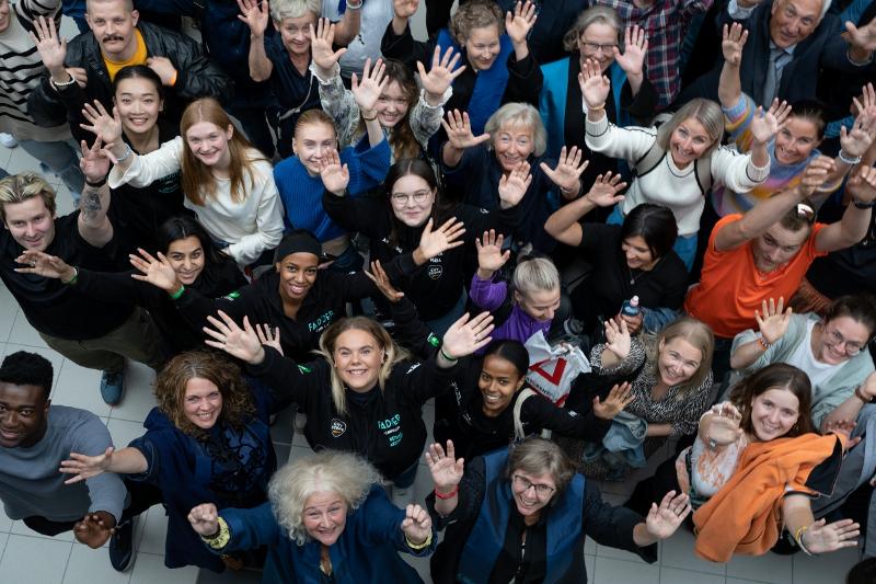En mengde studenter og ansatte vinker oppover og smiler stort. 