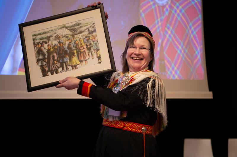 Ann_Ragnhild_Broderstad_UIT_20327_Foto_Stig_Brondbo.jpg Ei glad kvinne på ei scene held opp eit bilete/kunstverk. Ho er kledd i samsik kofte.