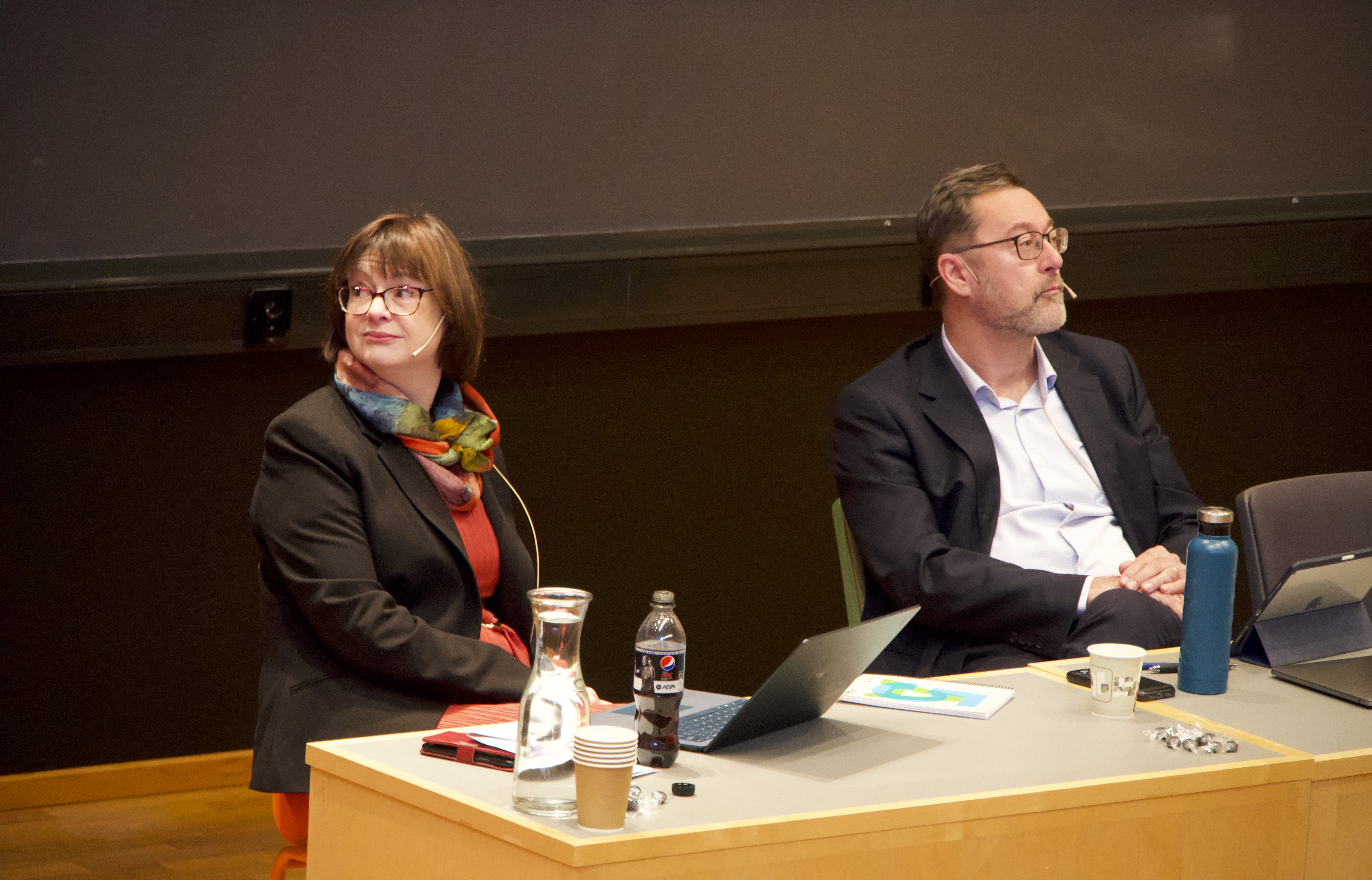 The two sitting next to each other listening to questions following their presentation. 