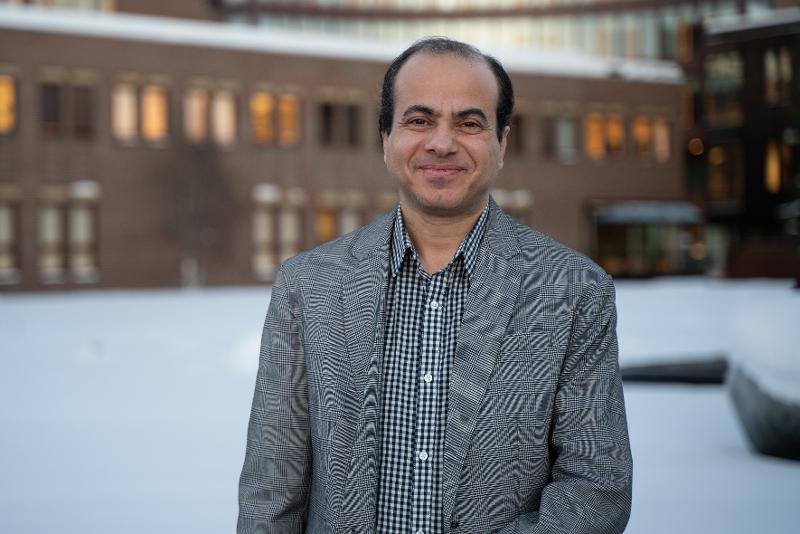 Ein smilande mann i dress, utand&oslash;rs om vinteren. Bygningar i bakgrunnen. 