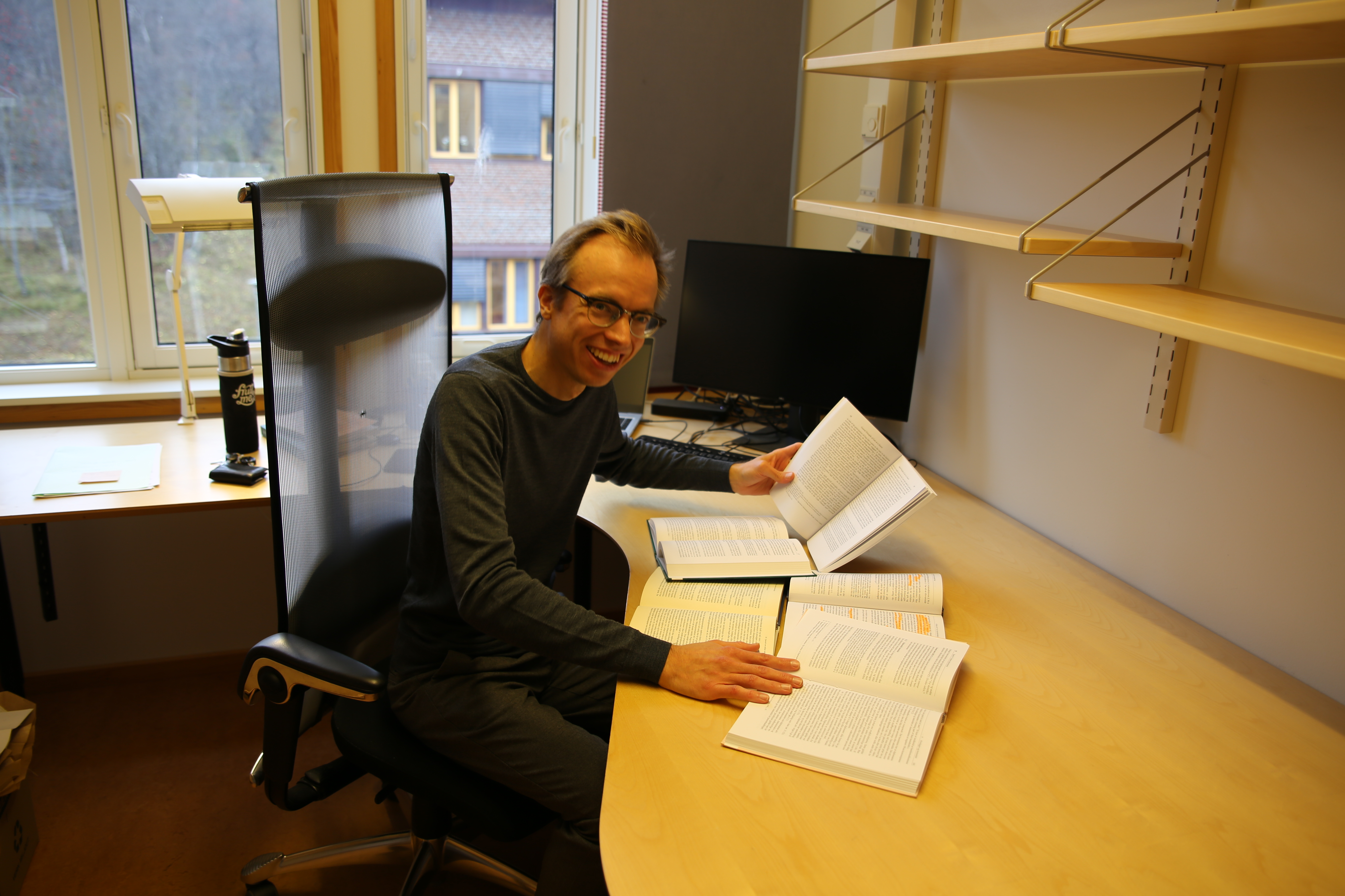 Sondre smiler og poserer på et ganske tomt kontor med et par bøker. 