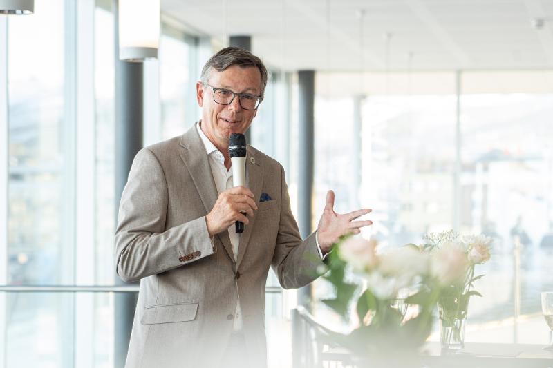 Mann i gr&aring; dress holder en tale. 