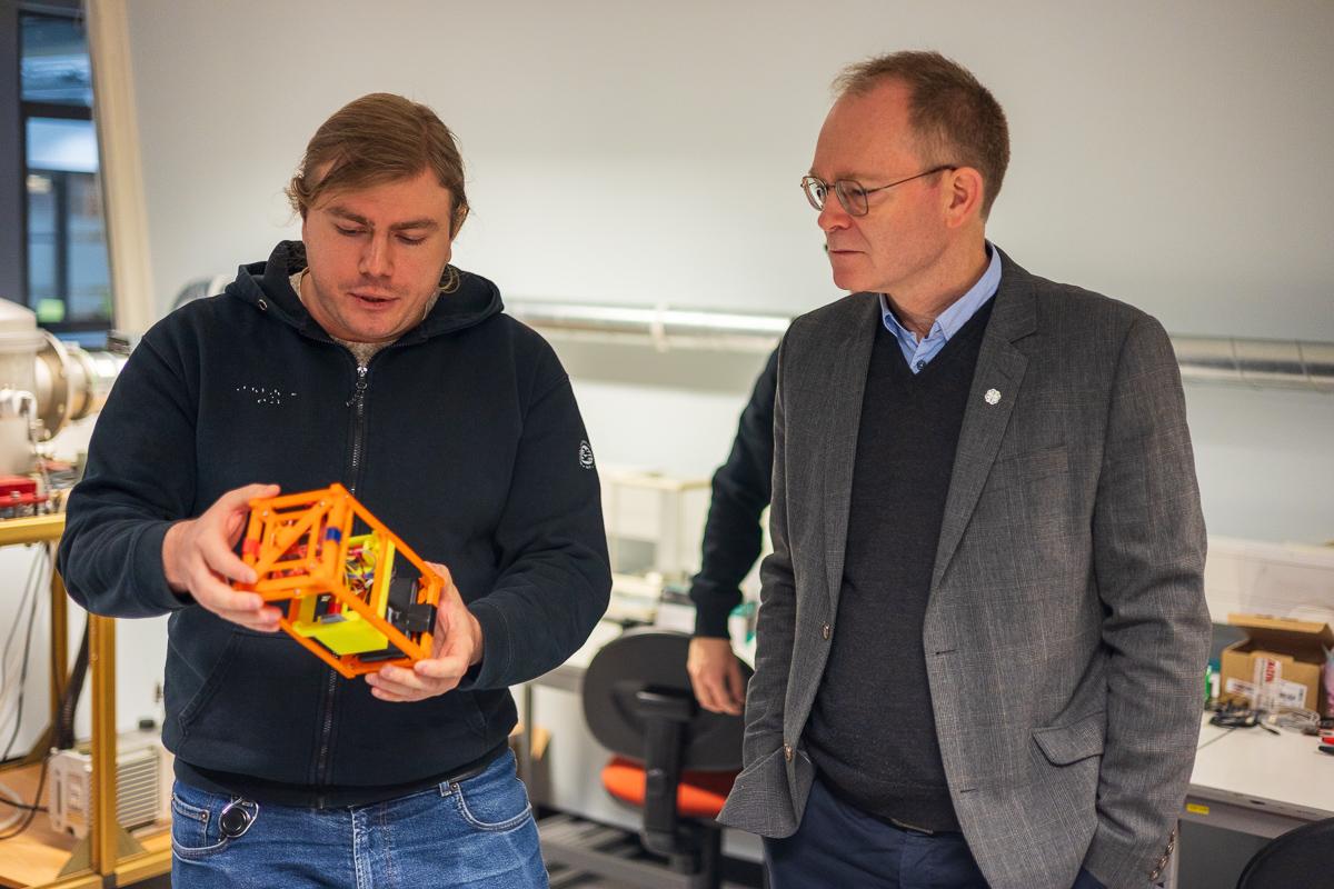 Forsknings- og h&oslash;yere utdanningsminister Oddmund Hoel (til h&oslash;yre) f&aring;r en innf&oslash;ring p&aring; laben av satelitteknologi-student Seweryn Roznowski ved UiT Narvik.