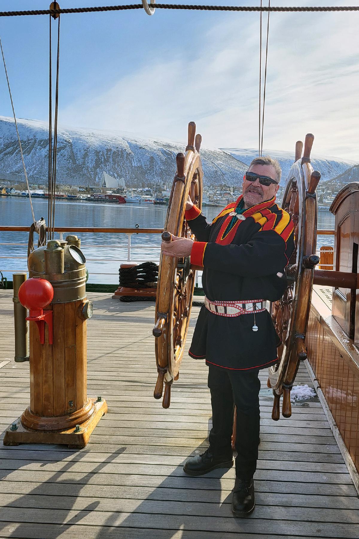 20250422_093409.jpg Mann i kofte står ved et ror om bord på en seilbåt.