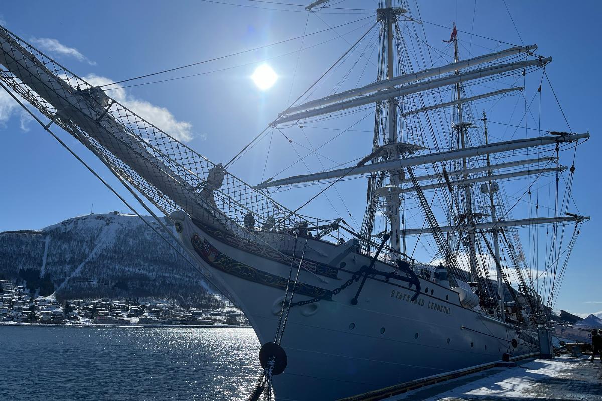 A sailing ship at port with a snow covered mountain behind.