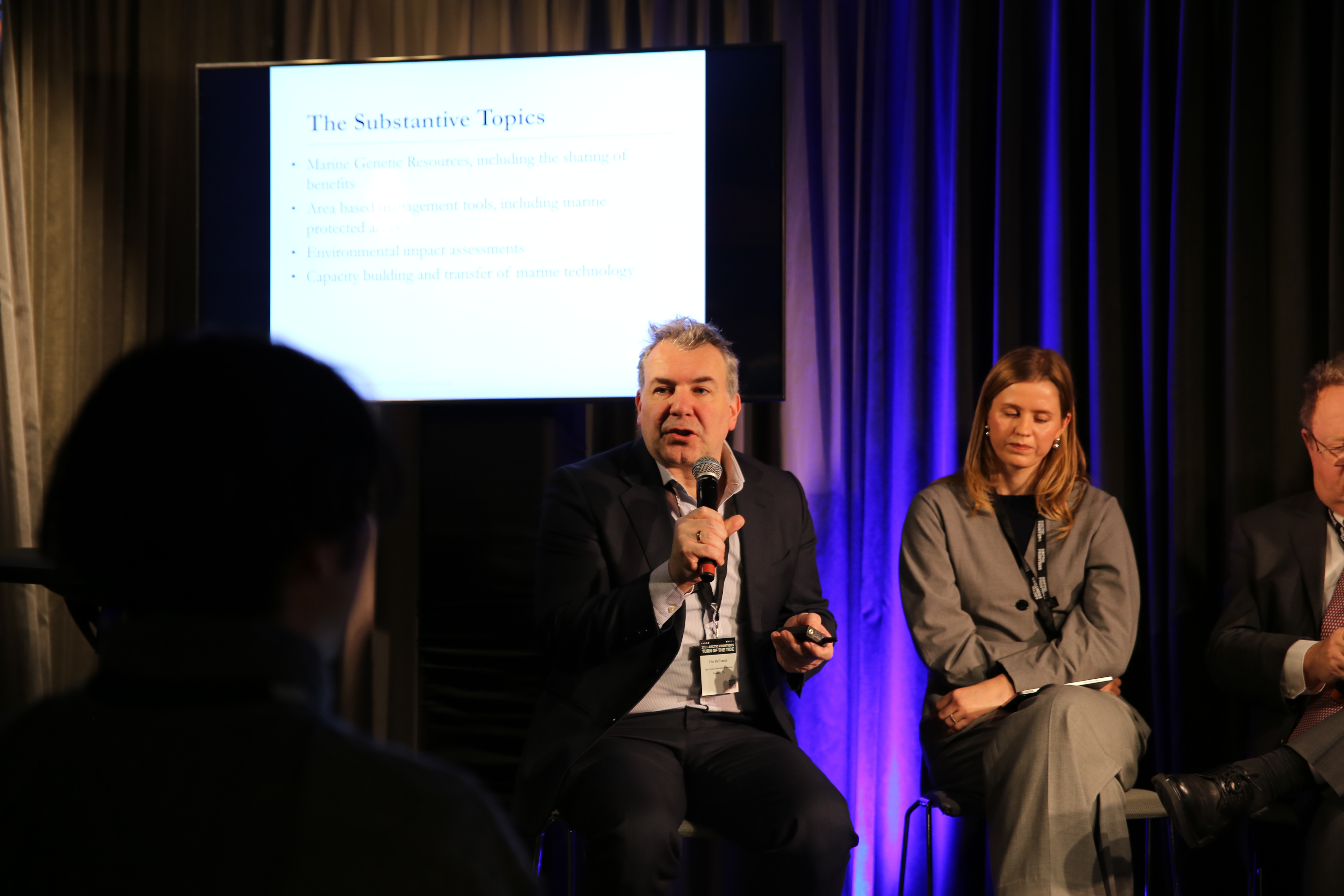 man, speaking, microphone, screen behind, dark room