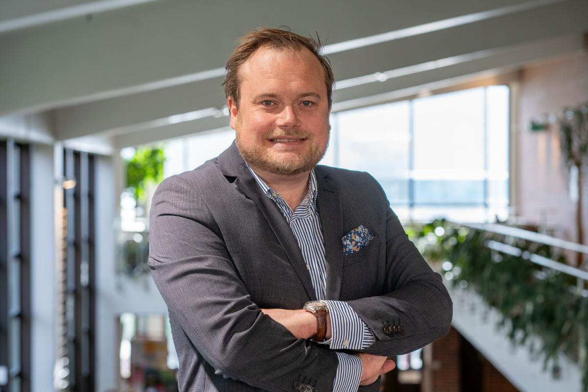 portrett av en smilende mann i dress med armene i kryss