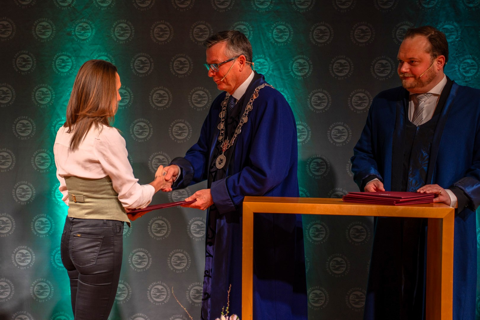 Kvinnelig forsker mottar pris av to rektorer. 