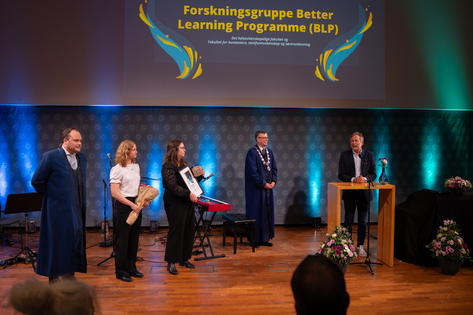 En mann og to kvinner har mottatt diplom, blomster og gave i staselig og feststemt universitetsauditorium. To rektorer st&aring;r p&aring; hver sin side av prisvinnerne. 